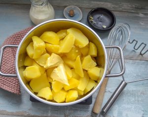 gekochte Kartoffeln mit Butter zu Püree stampfen
