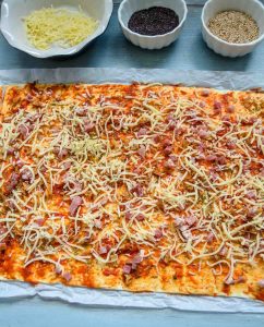 Blätterteig Platte mit Käse, Schinken und Röstzwiebeln belegen