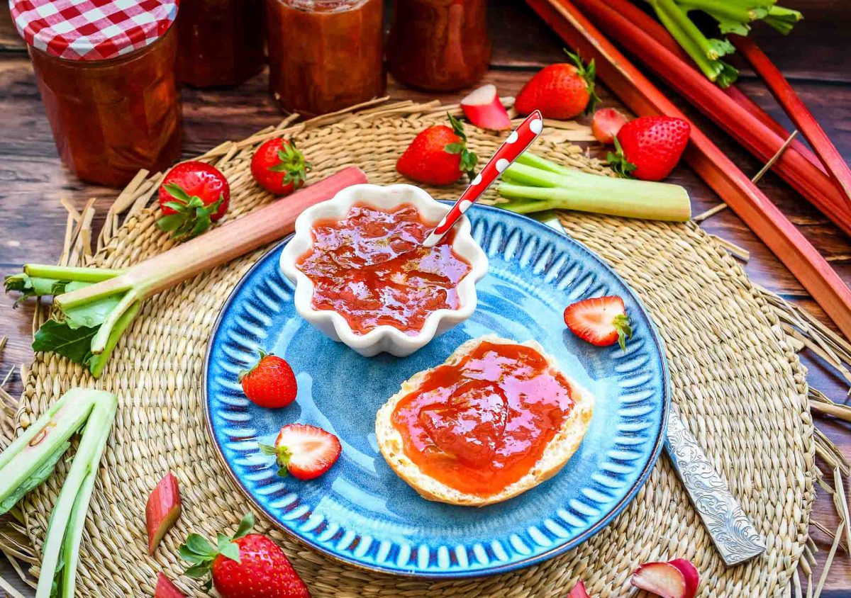 Omas  selbstgekochte Rhabarber Marmelade mit Erdbeeren und Vanille auf Brötchen Hälfte mit frischen Erdbeeren und Rhabarber 