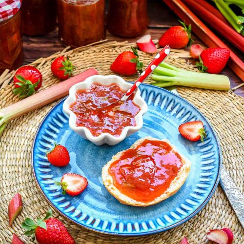 Omas selbstgekochte Rhabarber Marmelade mit Erdbeeren und Vanille auf Brötchen Hälfte mit frischen Erdbeeren und Rhabarber