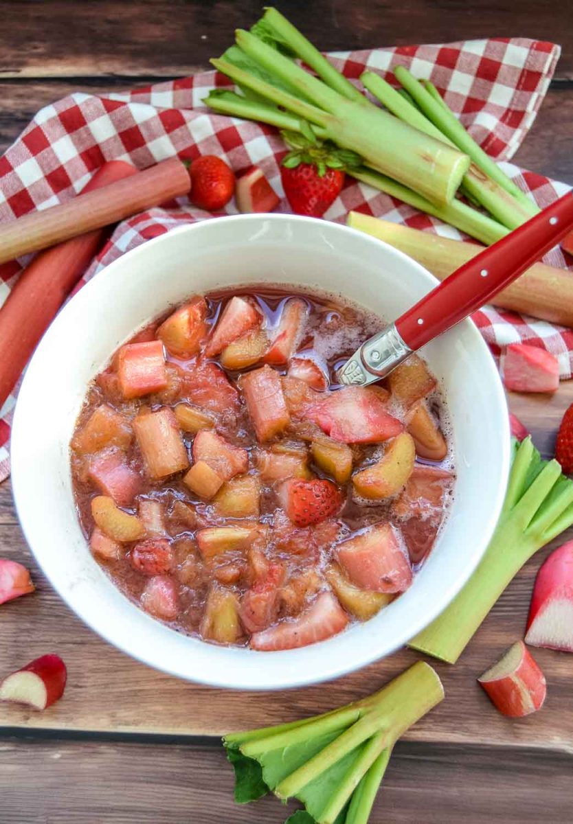 Omas leckerer fruchtiger Rhabarberkompott mit Vanille und Erdbeeren in weißer Schüssel mit Löffel