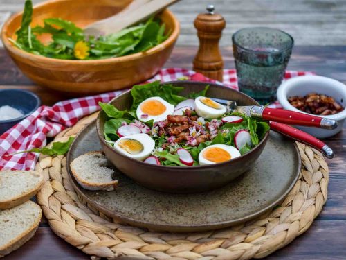 Löwenzahnsalat nach Omas Rezept mit Ei und Speck im tiefen Teller angerichtet mit Brot