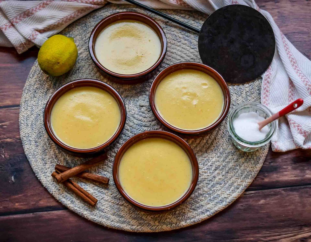 spanische Crema Catalana mit geriebener Zitronenschale und Zimt in kleiner brauner Tonschale mit Brenneisen und Zucker zum karamellisieren