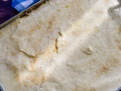 Bechamelsoße auf den griechischen Auflauf mit Kartoffeln und Hackfleisch gießen